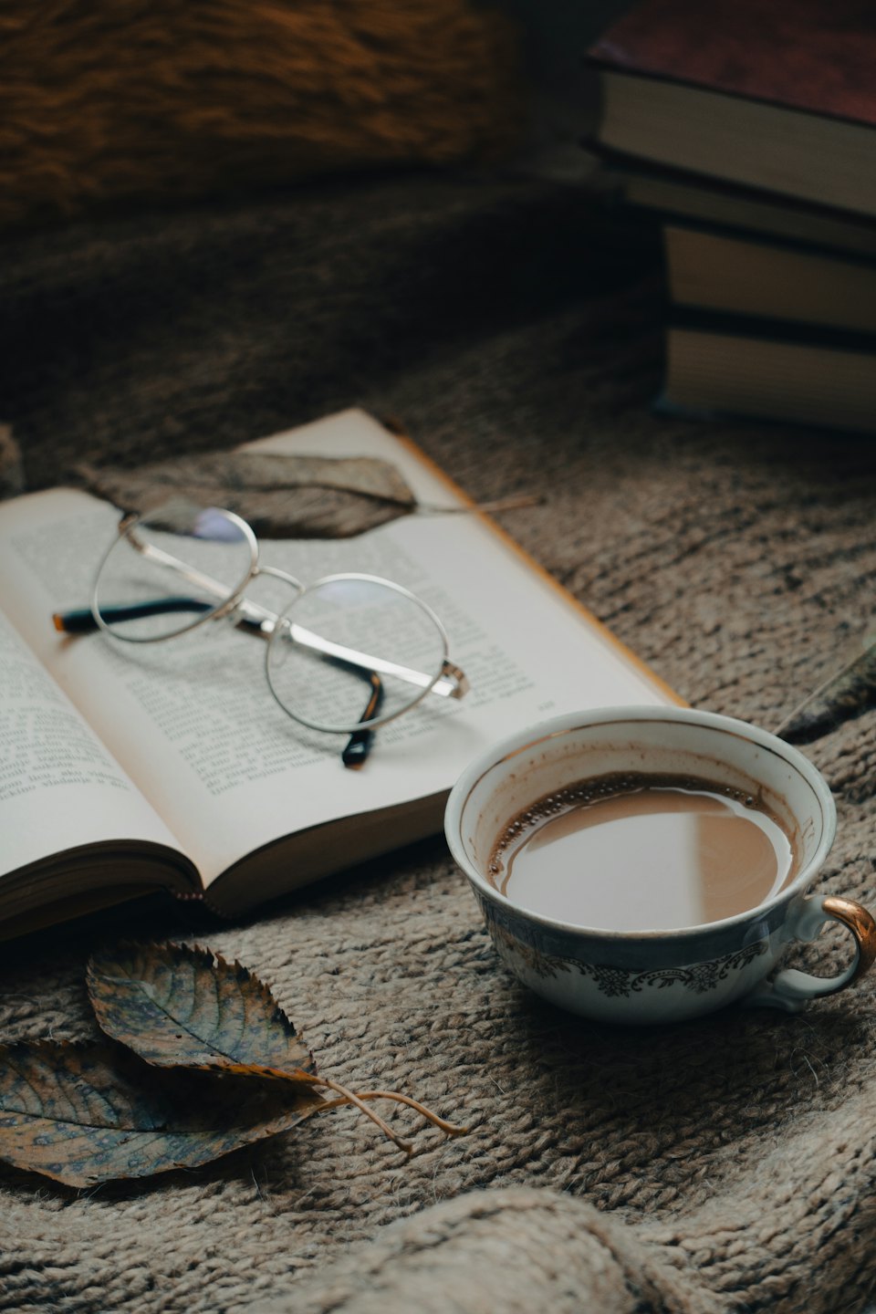 Libro aperto, occhiali e caffè su una coperta di lana.