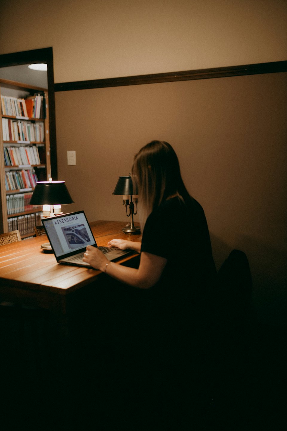Persona che lavora al computer portatile su una scrivania di legno con lampade.